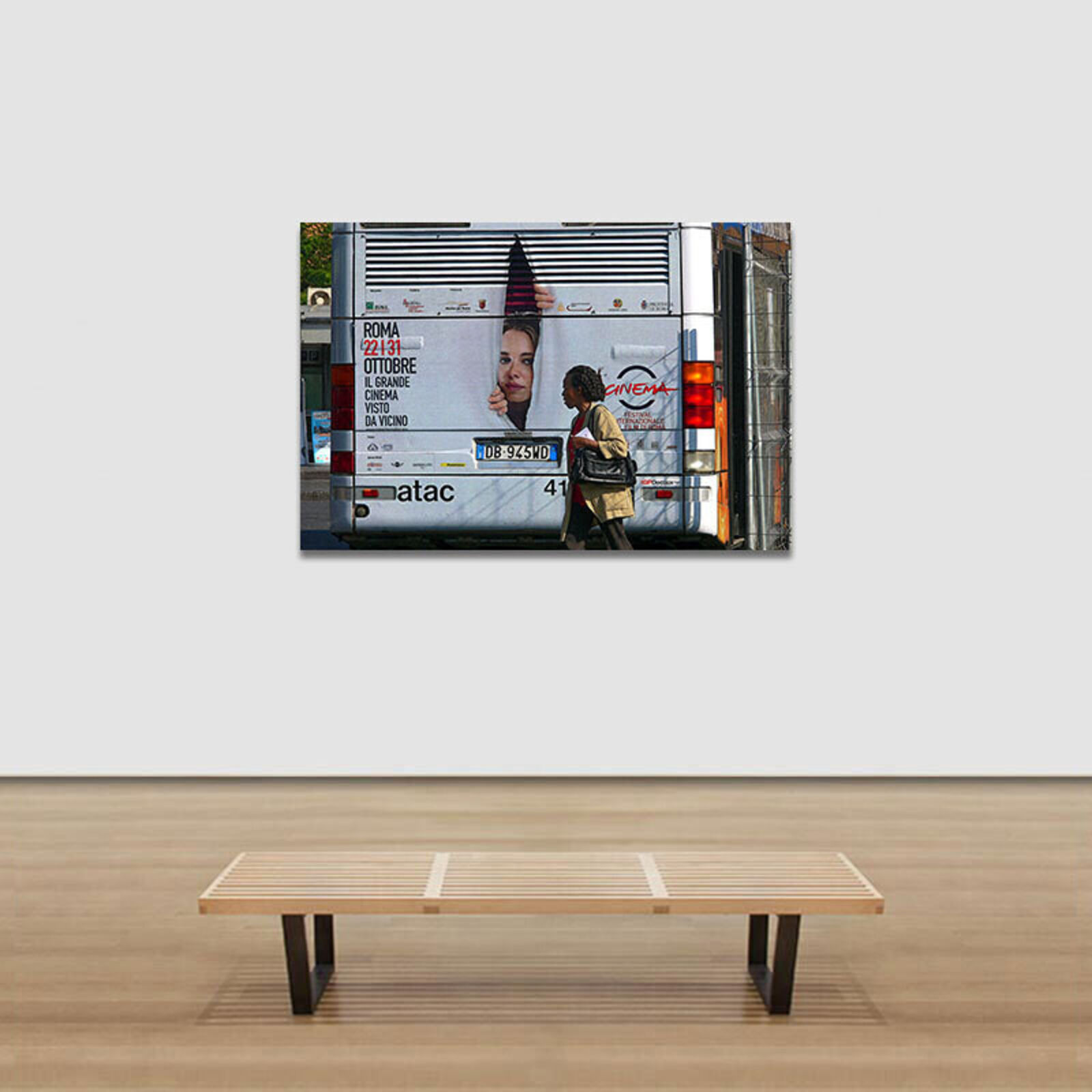 A woman walking past a bus with a poster on the back.