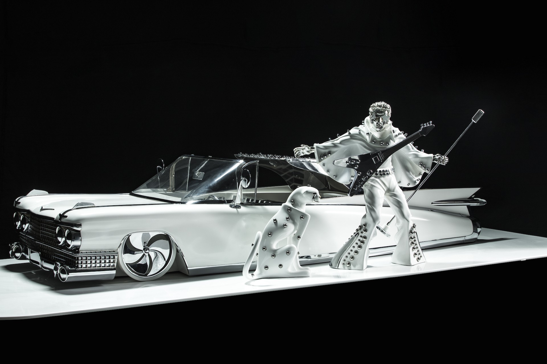A statue of Elvis Presley standing next to a white car.