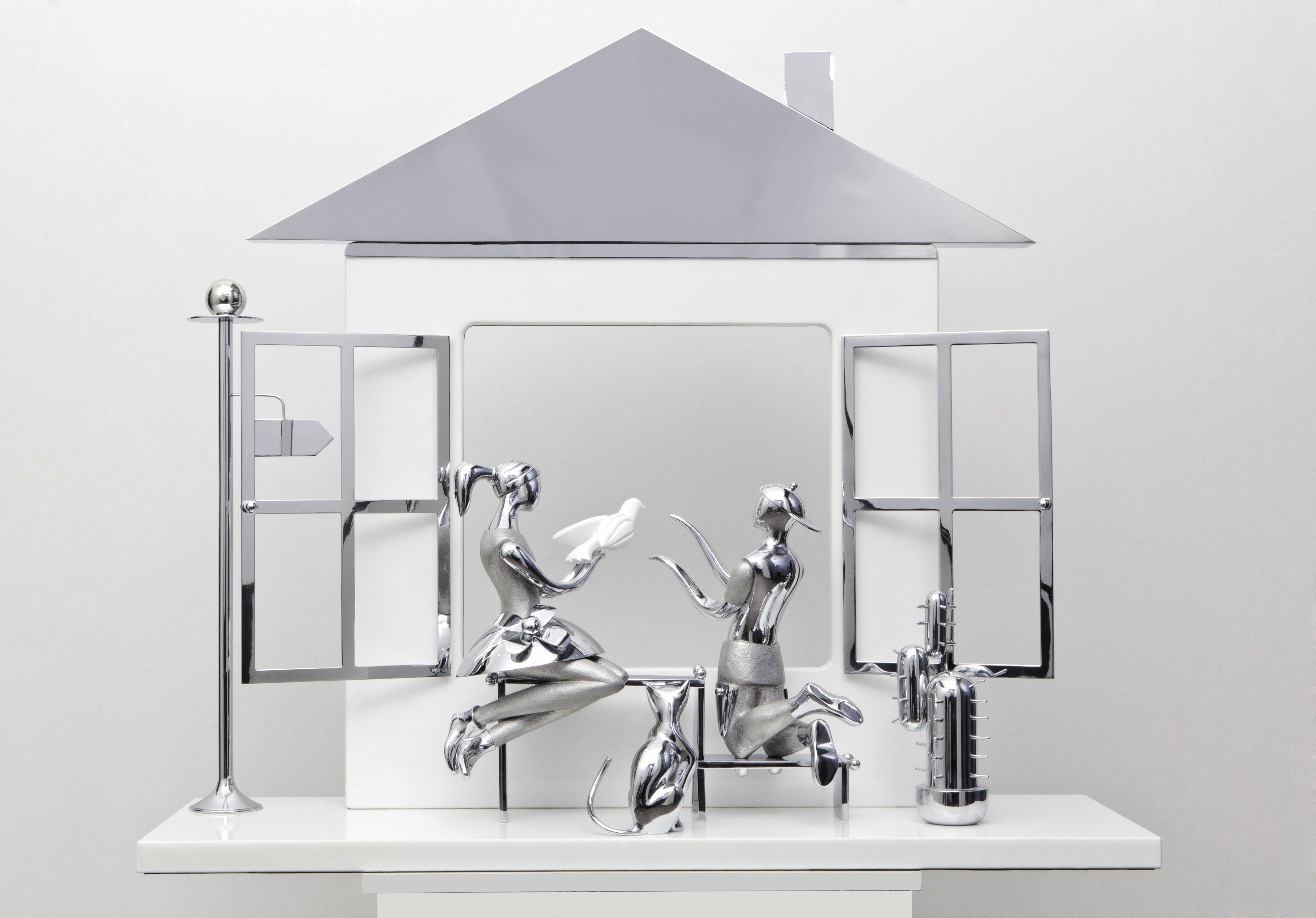 A silver figurine of a woman sitting on a shelf in front of a mirror.