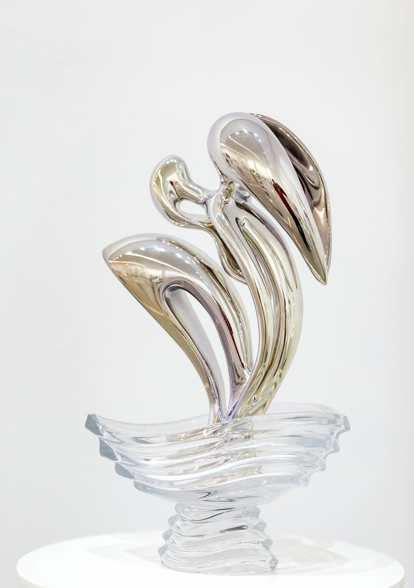 A silver sculpture of two swans on a glass pedestal.