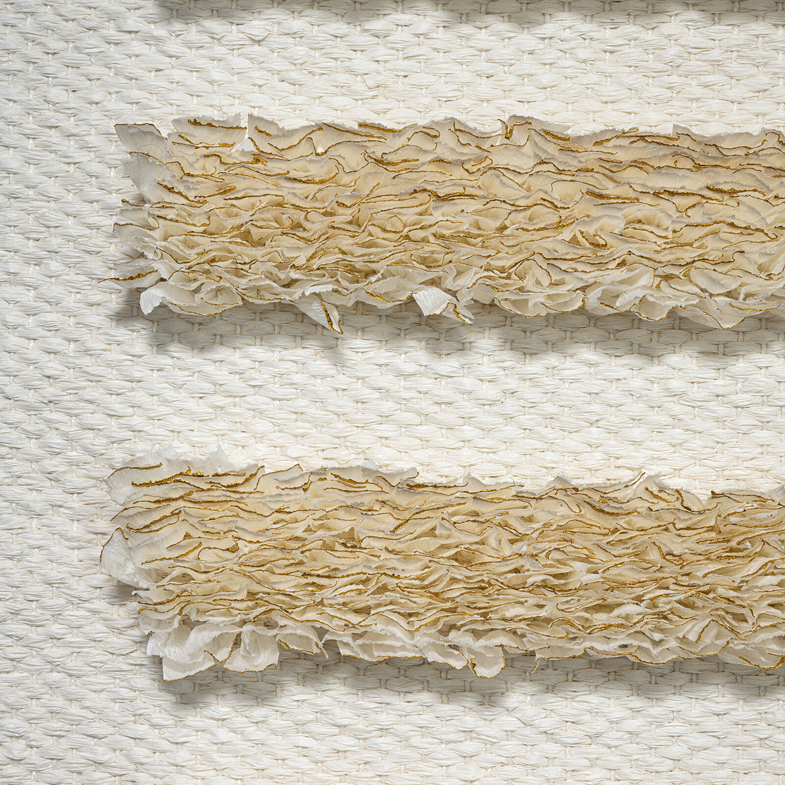 A minimalist textile piece featuring a woven white background with horizontal strips of textured, golden-brown fibers.