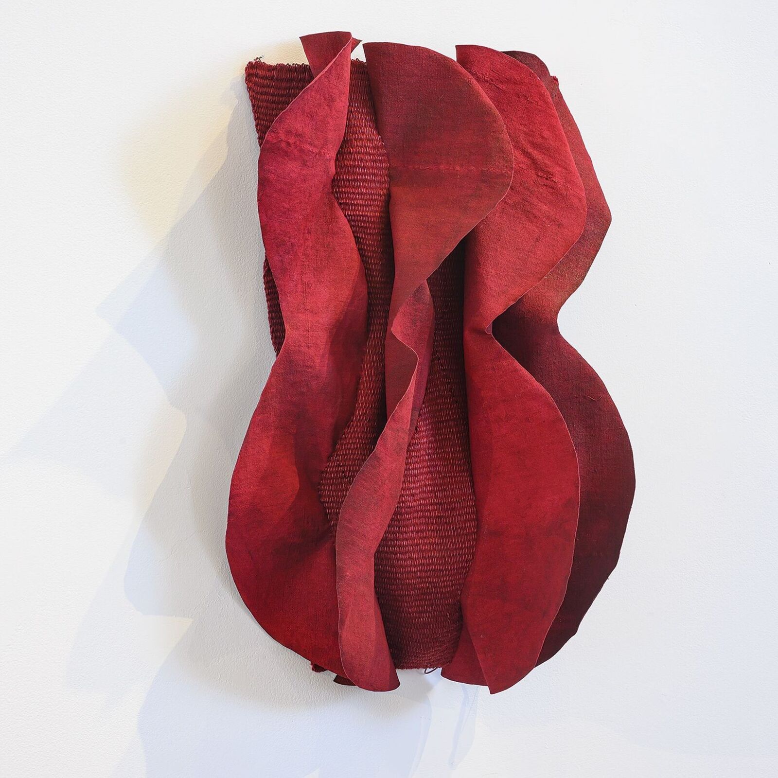 A red sculpture on a white wall with a white background.