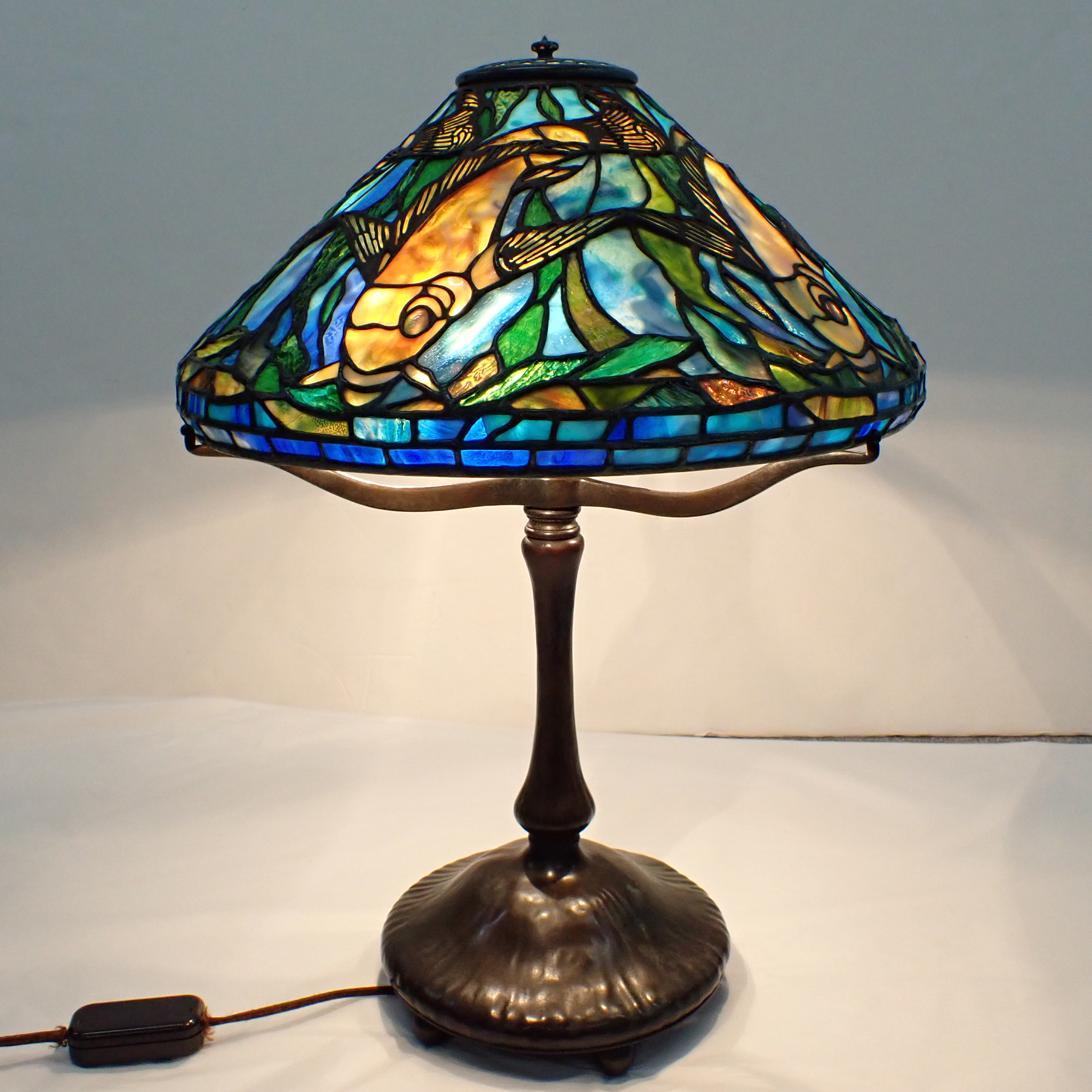 A stained-glass table lamp featuring a vibrant underwater scene with fish and aquatic plants.