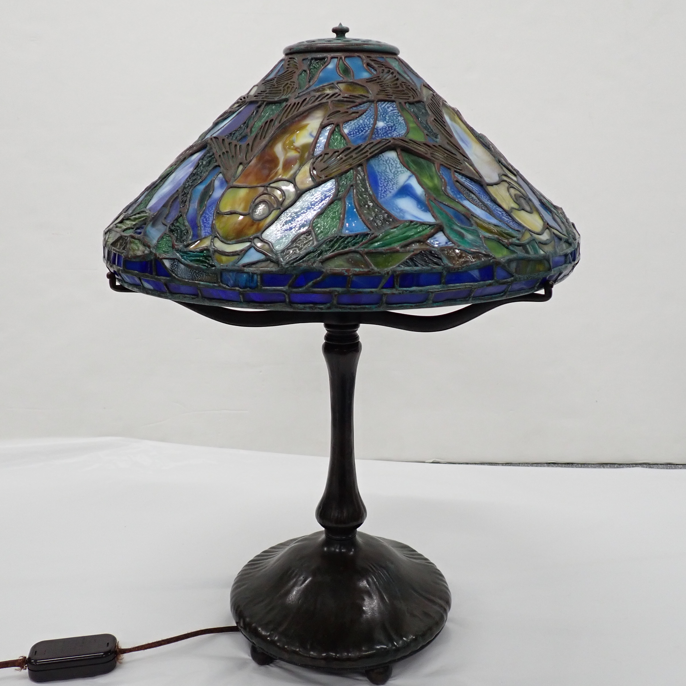 A stained-glass table lamp featuring a vibrant underwater scene with fish and aquatic plants.