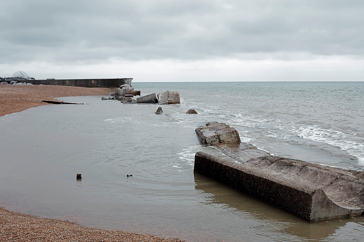 A beach with rocks in the water and a pier in the background.