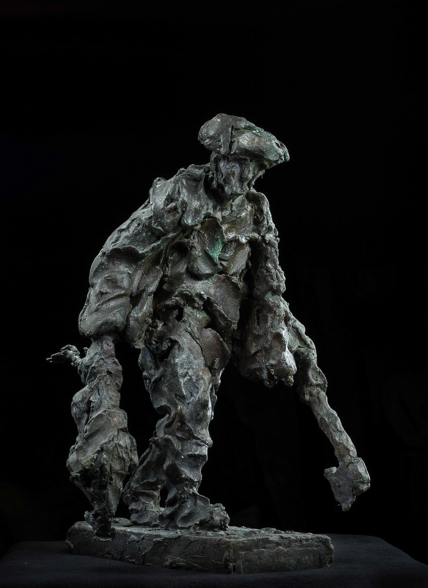 A rough, textured bronze sculpture of a figure in a hat holding an axe against a black background.