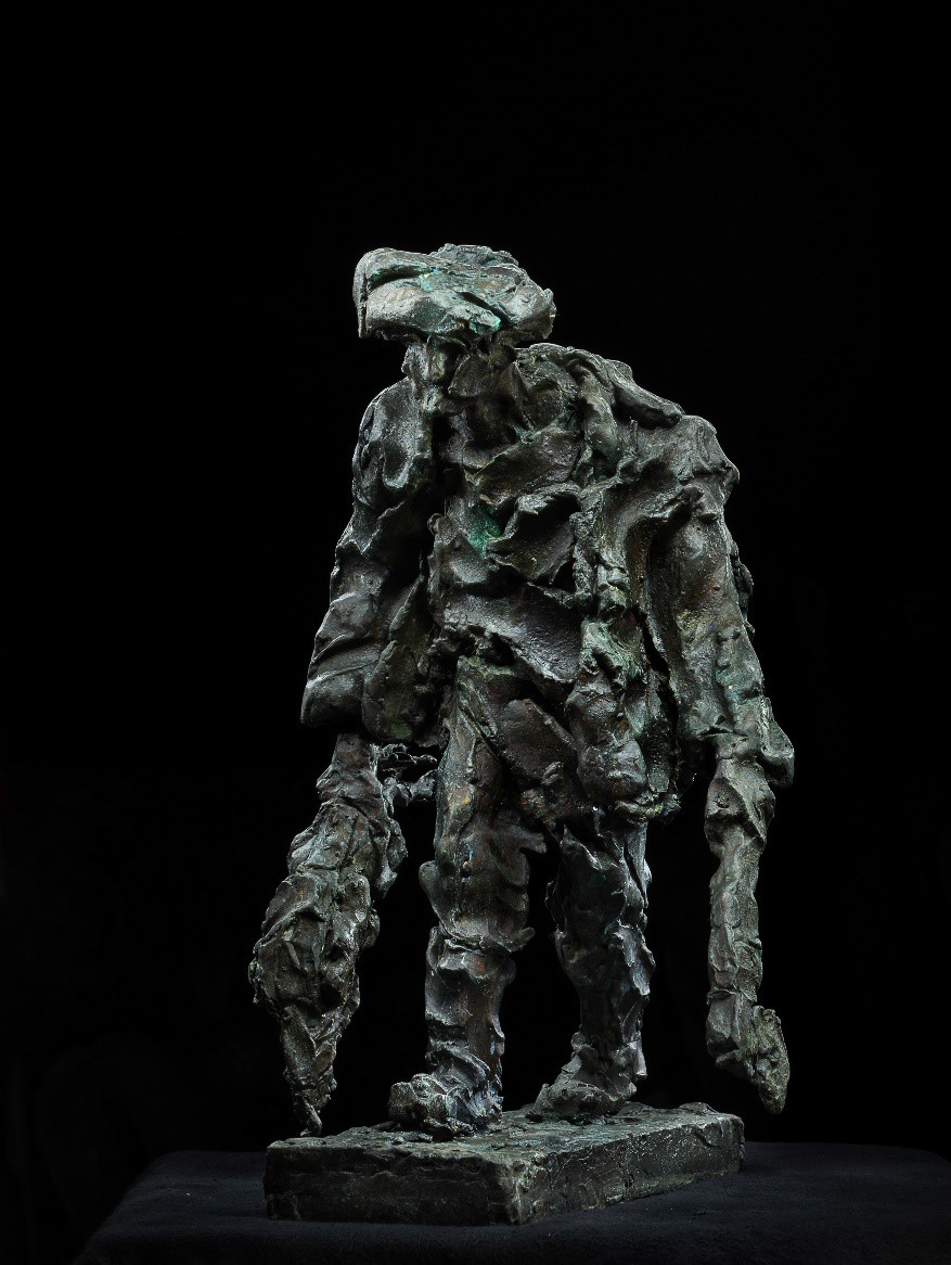 A rough, textured bronze sculpture of a figure in a hat holding an axe against a black background.