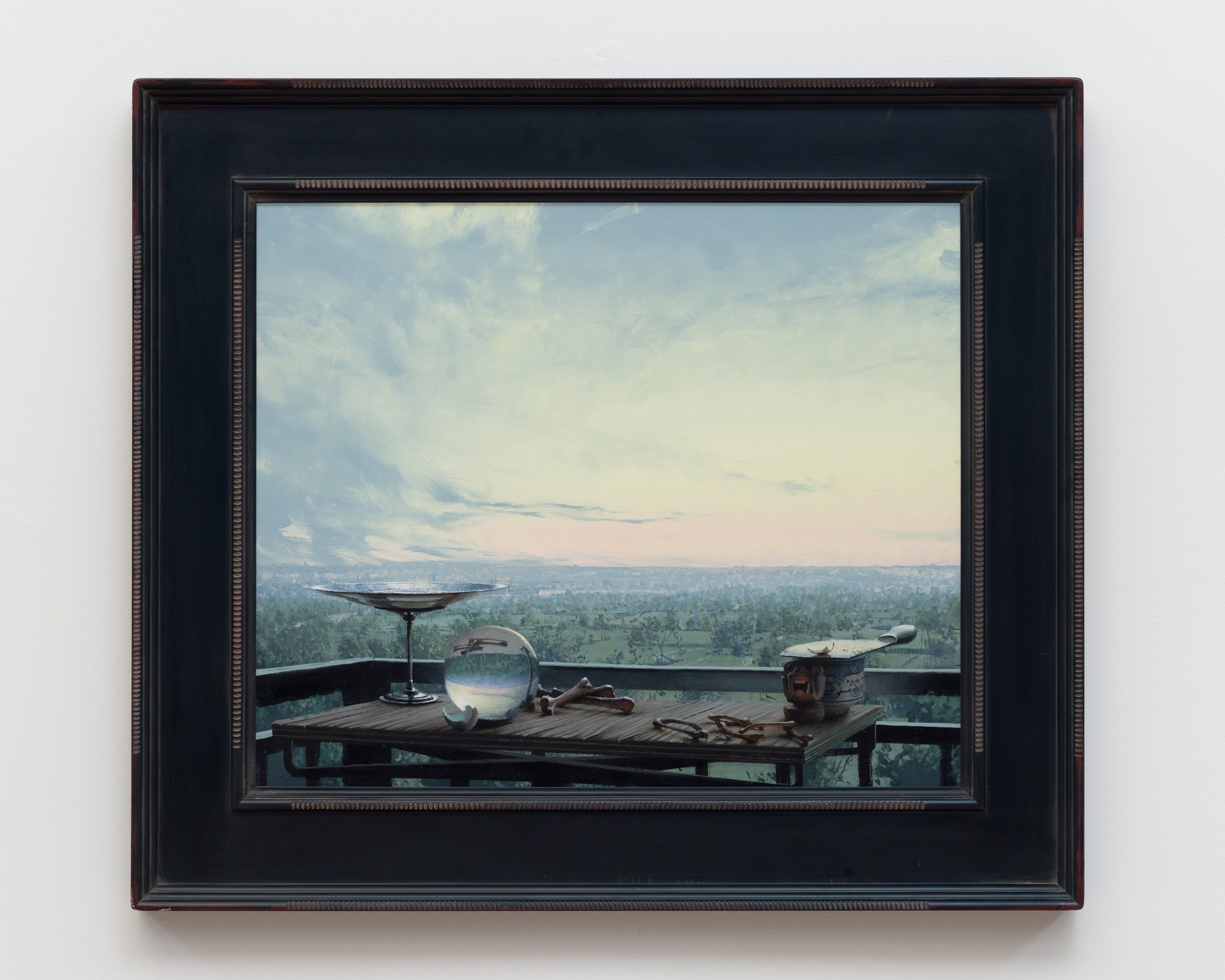A still life arrangement of eclectic objects on a wooden table overlooking a vast, hazy landscape.