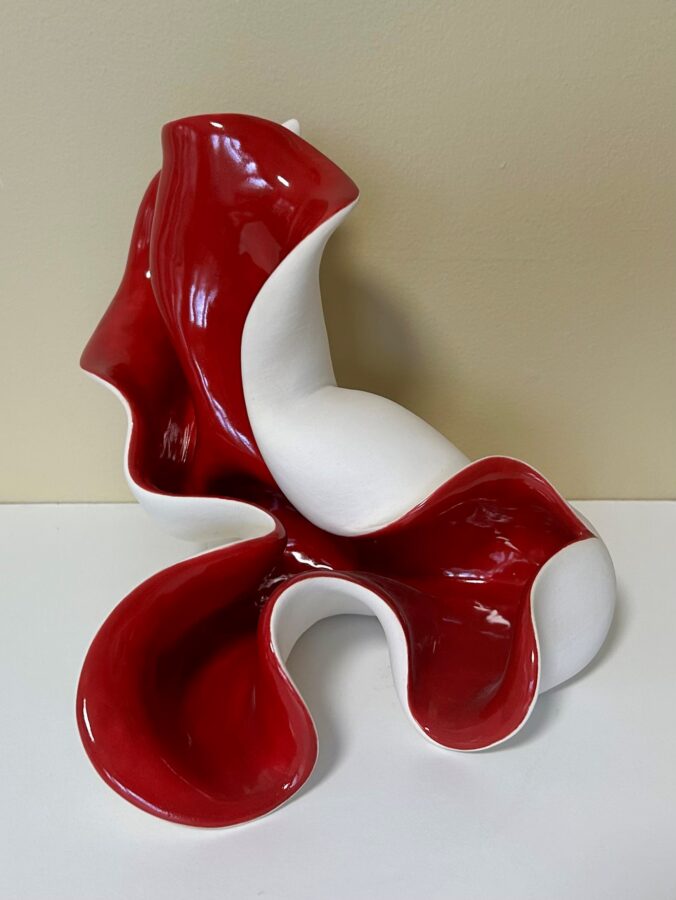 A glossy ceramic sculpture featuring a bold red and white color scheme with fluid, organic forms.