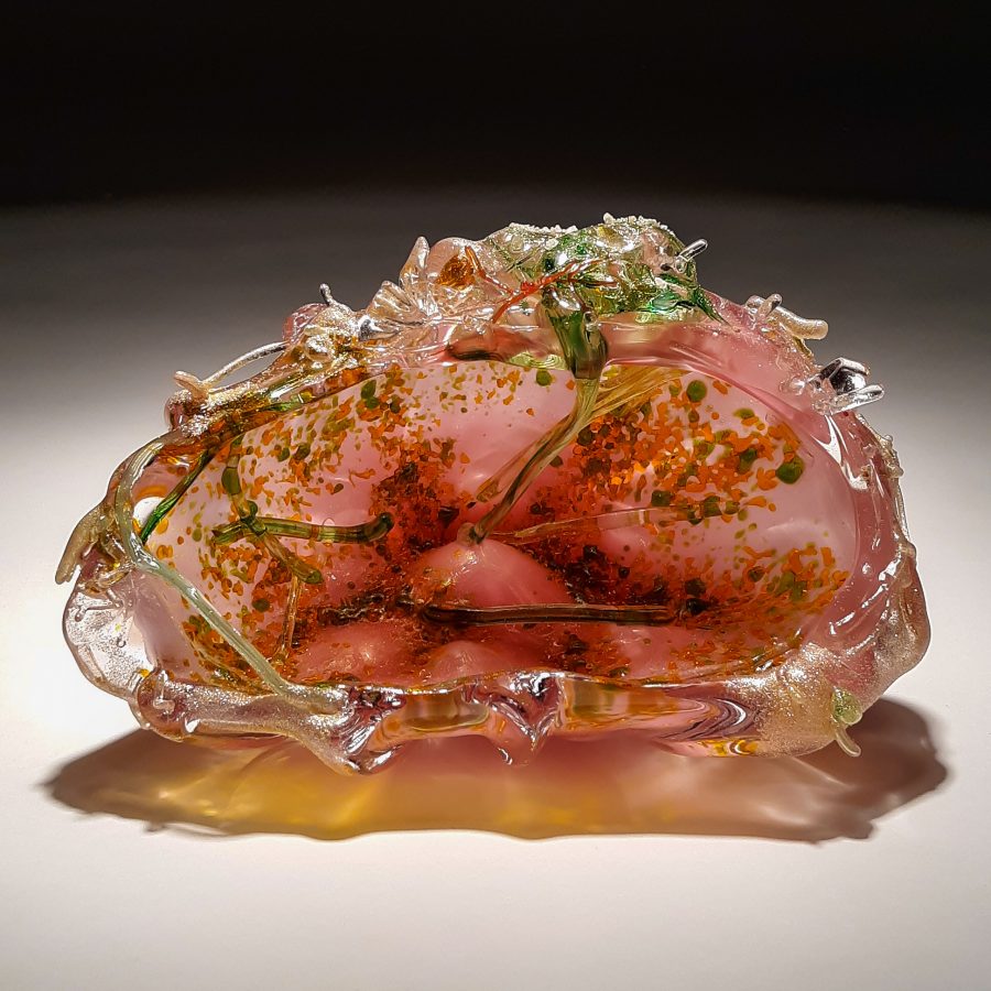A translucent pink glass sculpture resembling a shell filled with suspended organic elements.