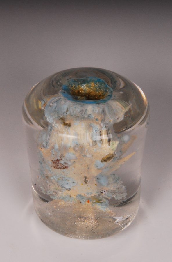 A clear glass paperweight featuring an abstract, organic form with metallic inclusions.