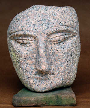 A serene stone sculpture of a face with closed eyes resting on a wooden base.