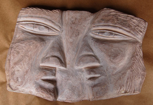 A carved wooden mask featuring a symmetrical face with expressive eyes and textured hair.