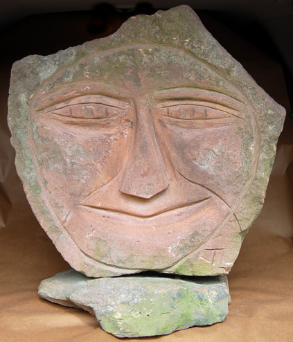 A weathered stone sculpture of a smiling face resting on a base.