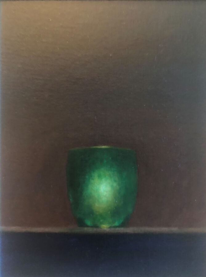A solitary green glass object rests on a dark surface.