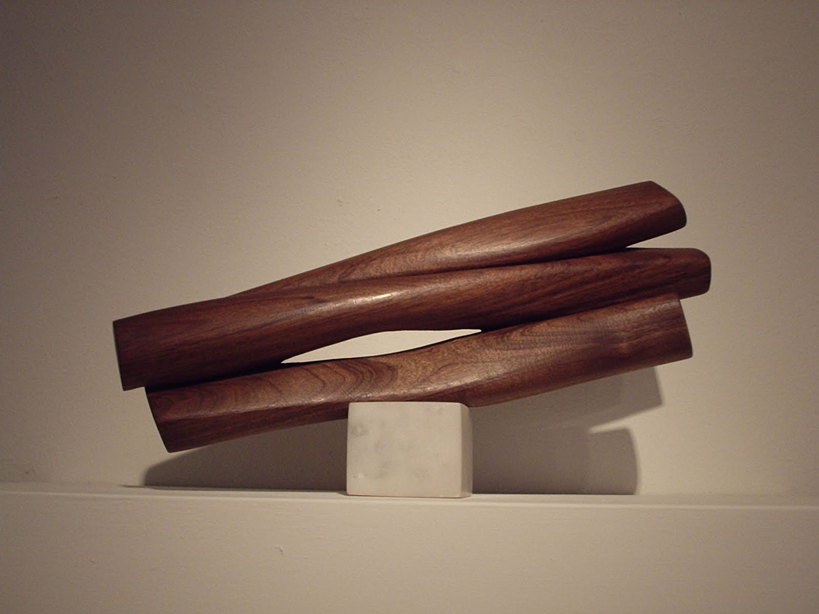 A wooden sculpture on a white shelf with a white marble base.