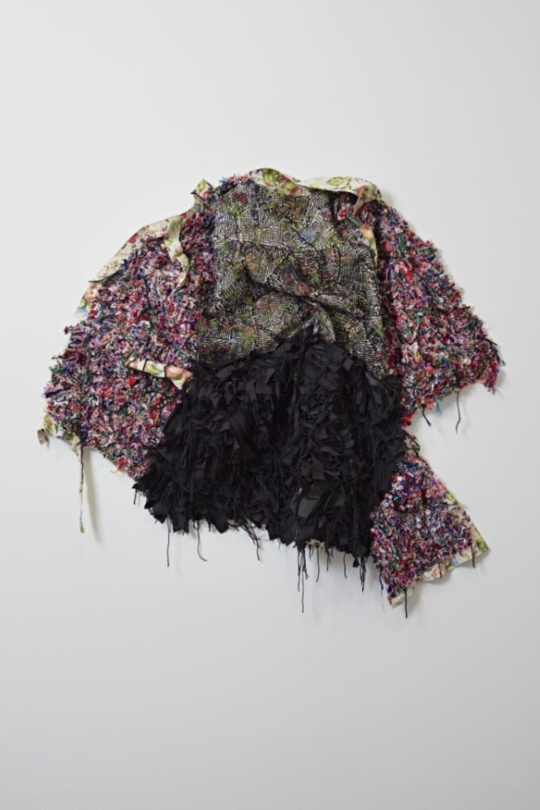 A textured, abstract textile sculpture mounted on a plain white wall.
