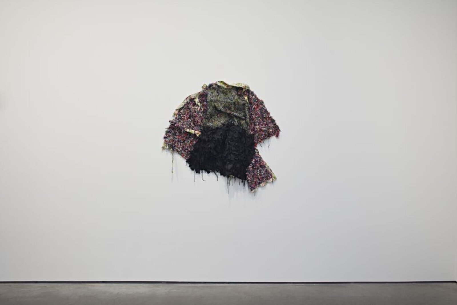 A textured, abstract textile sculpture mounted on a plain white wall.