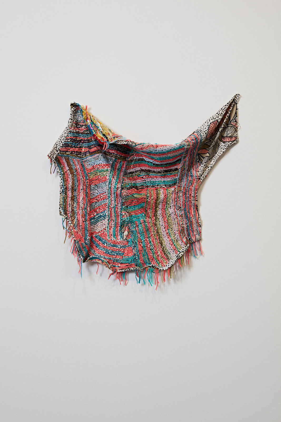A multicolored shawl hanging on a white wall. 