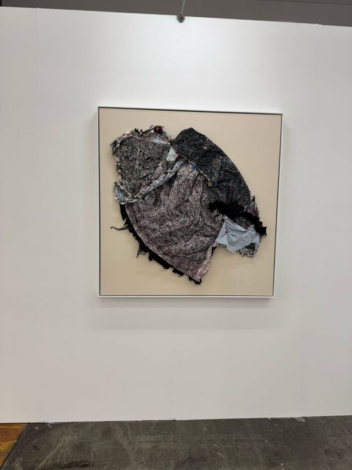 A person stands in a gallery space looking up at a framed textile artwork.