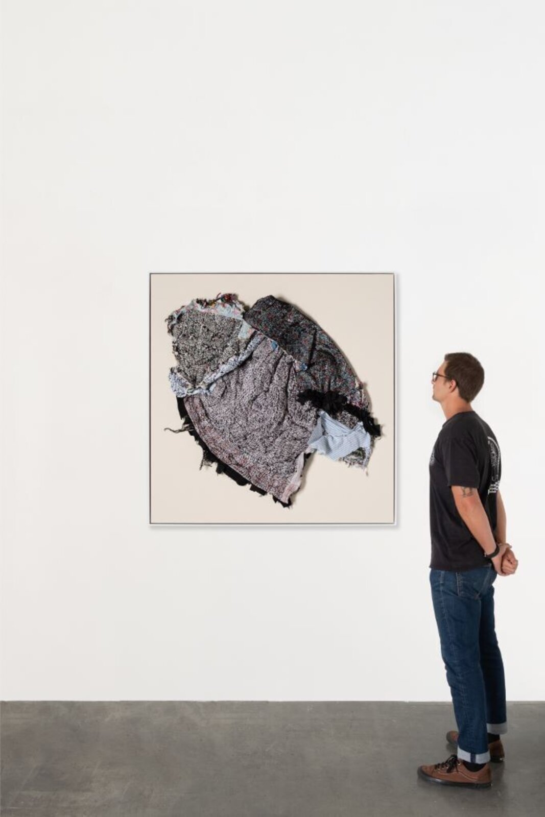 A person stands in a gallery space looking up at a framed textile artwork.
