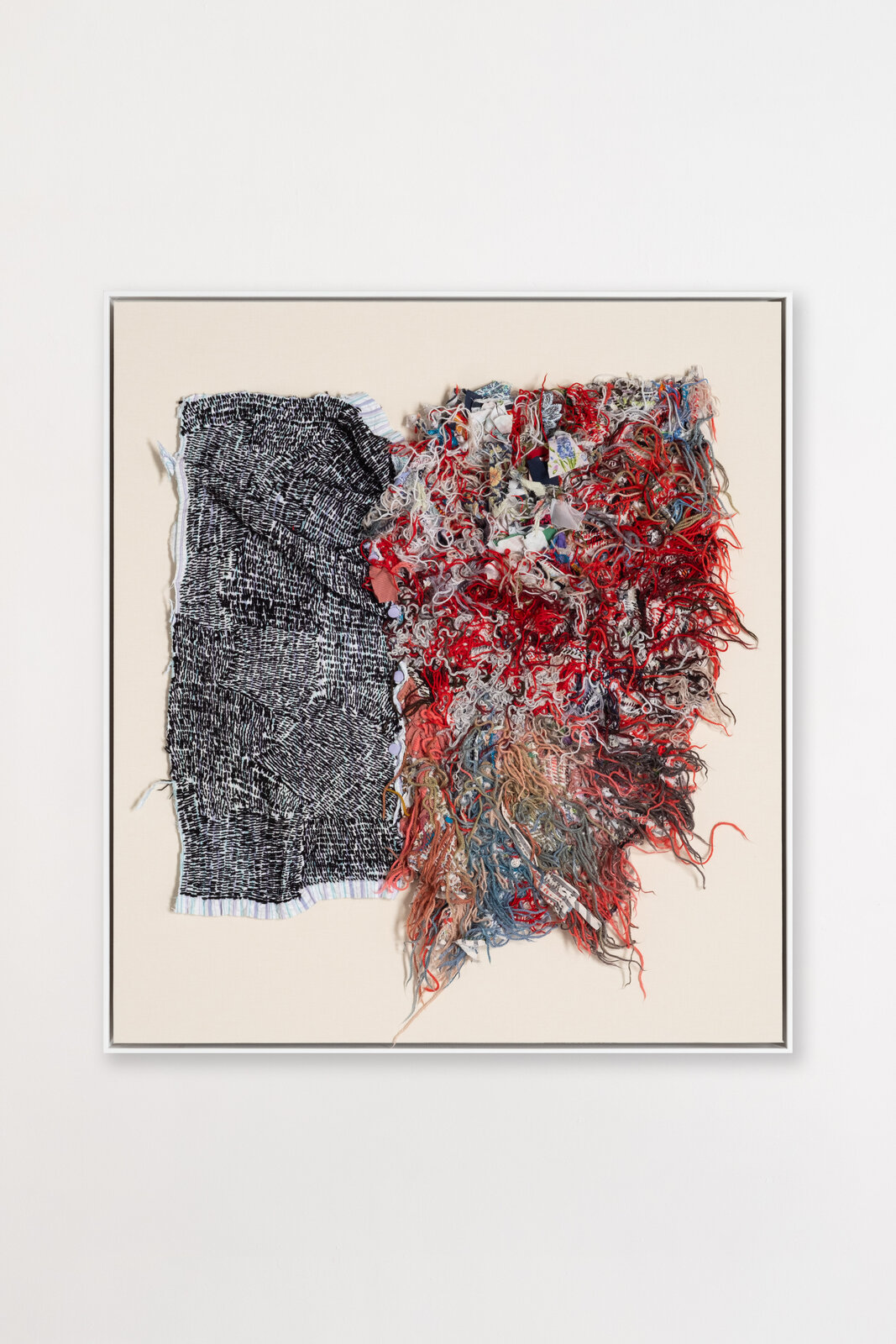 A textile artwork featuring a black-and-white woven panel next to a chaotic, colorful pile of loose threads and fabric scraps.