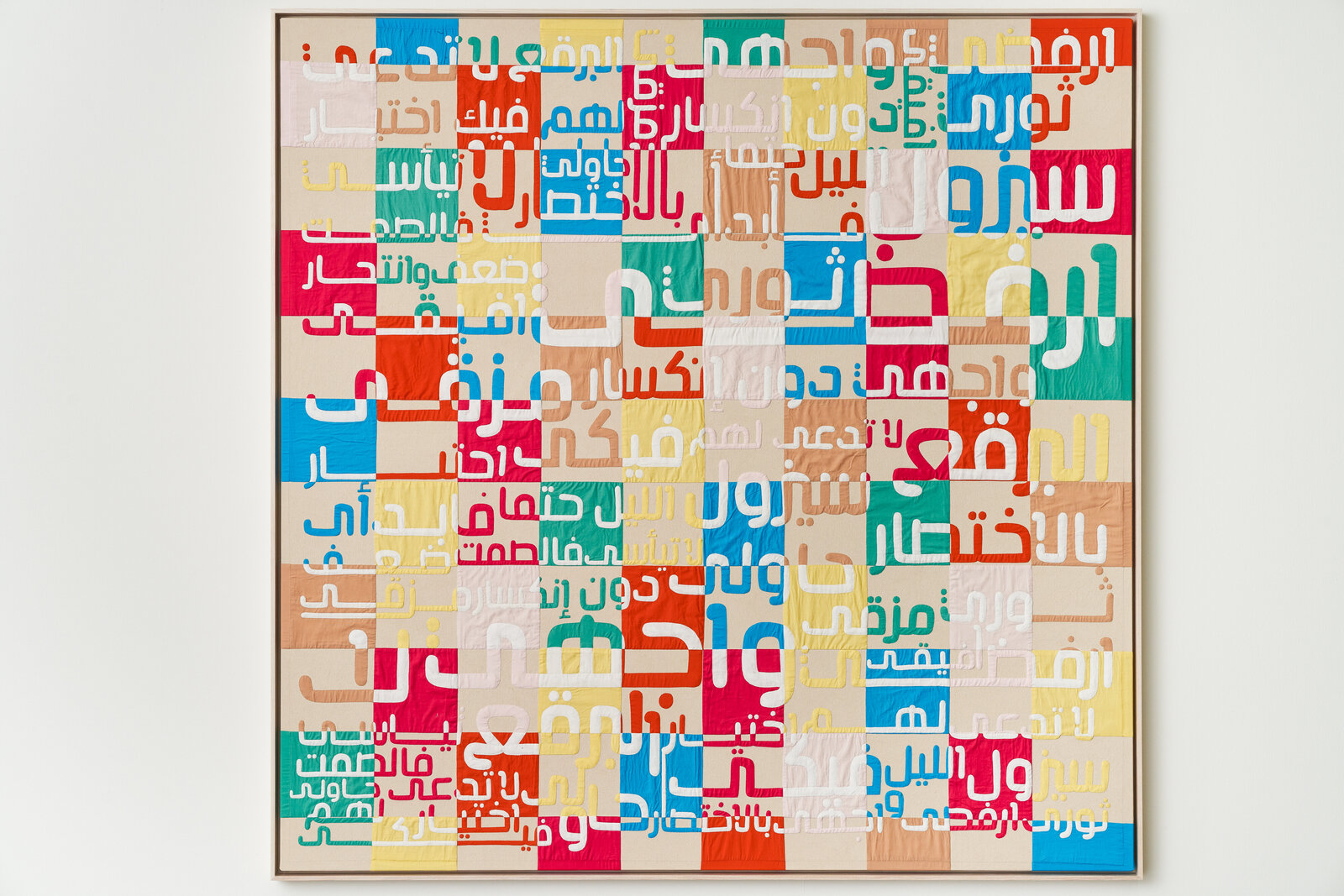 A colorful quilt with arabic writing on it on a white wall.