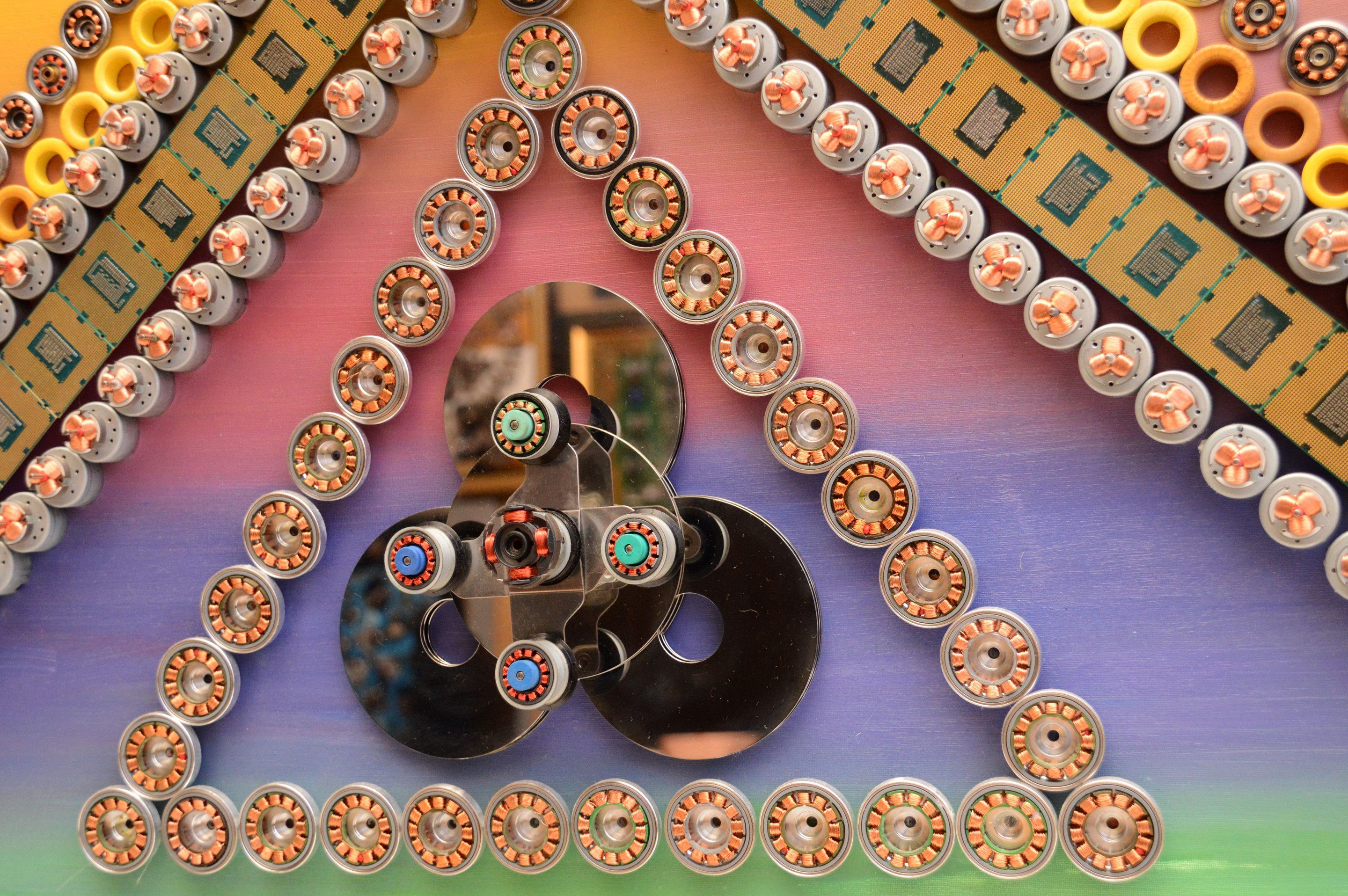 A macro photograph of a metallic gear surrounded by yellow rings and green circuit boards.