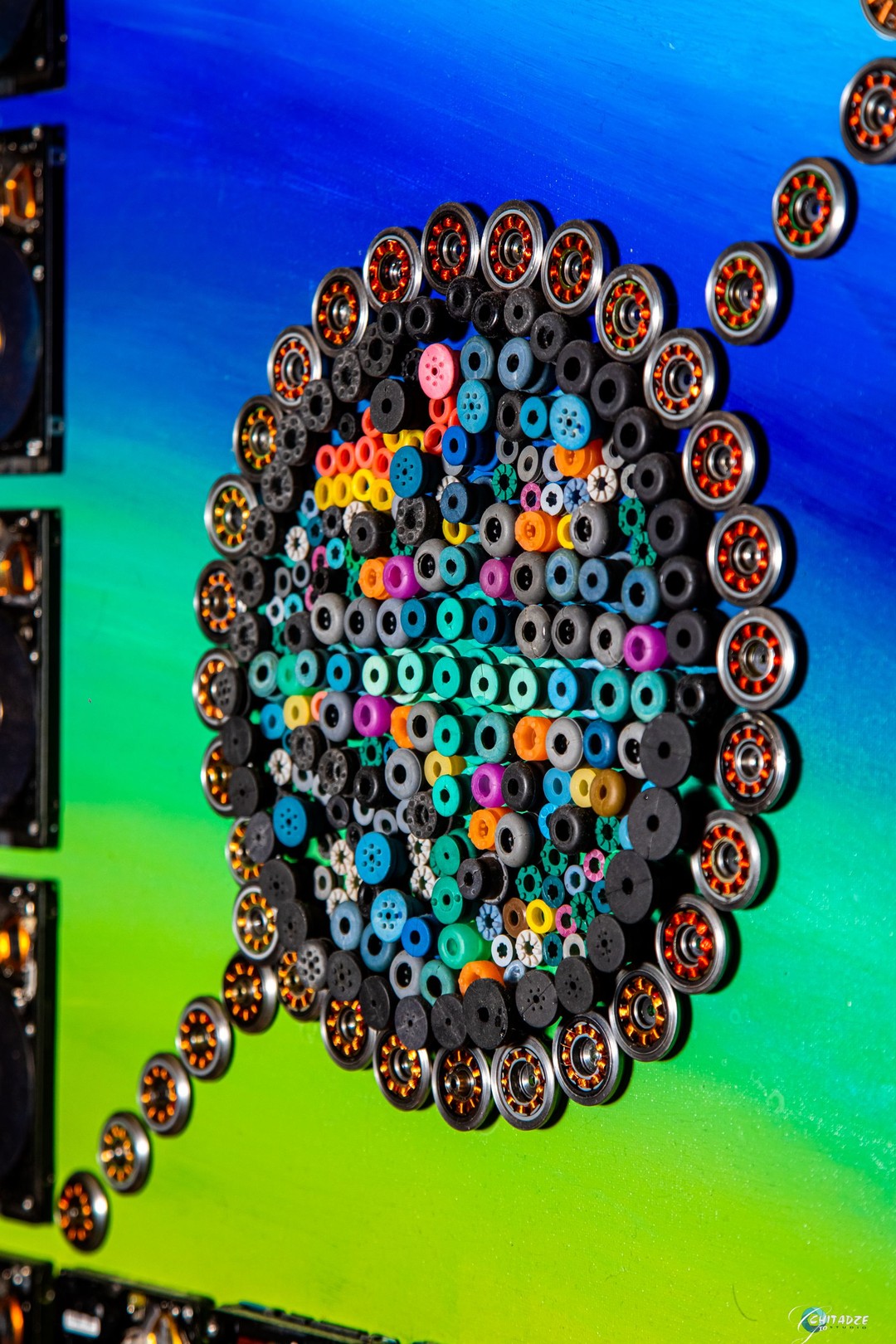 A circular arrangement of metallic discs surrounding a central dark cluster, set against a vibrant blue and green background.