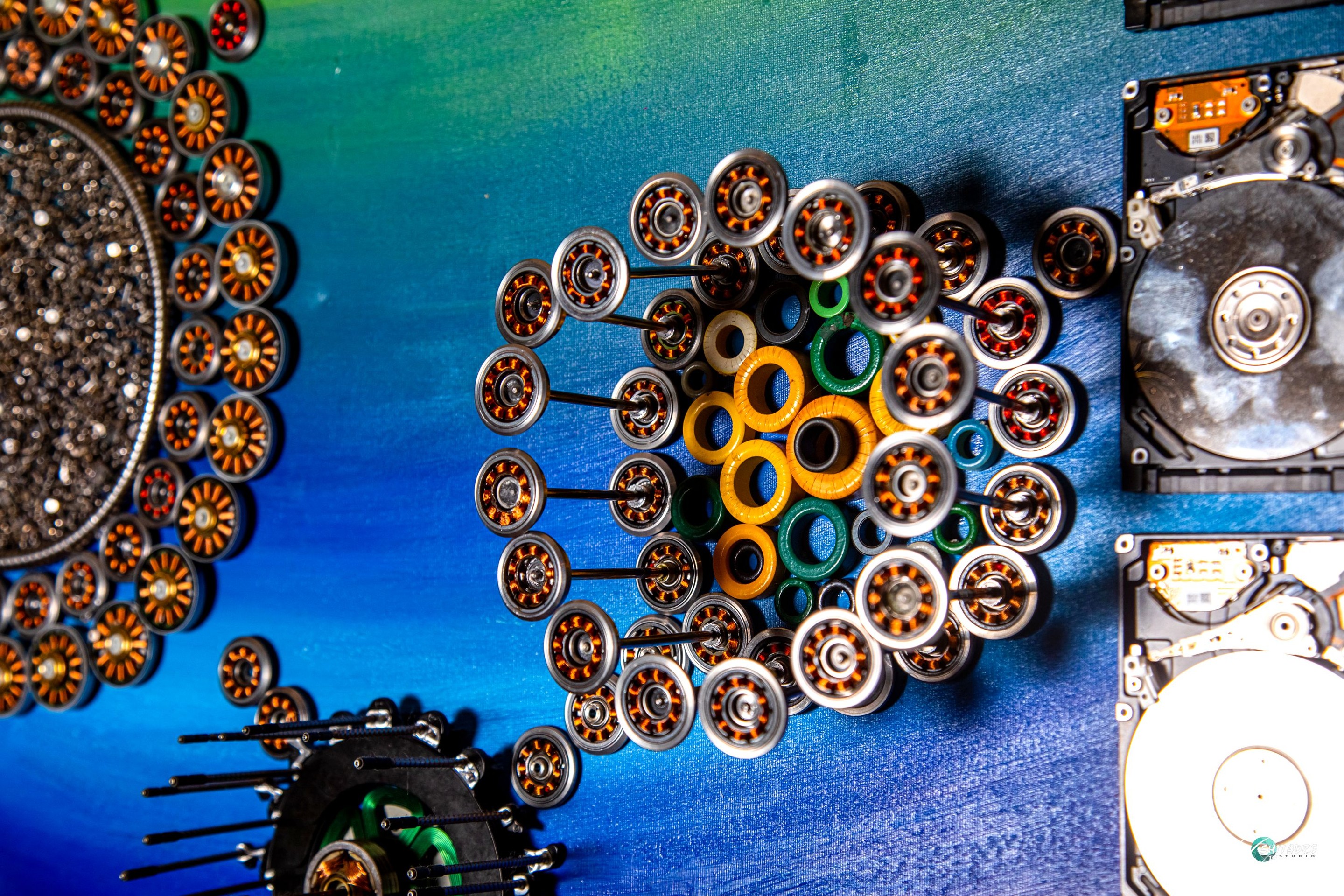 A circular arrangement of metallic discs surrounding a central dark cluster, set against a vibrant blue and green background.