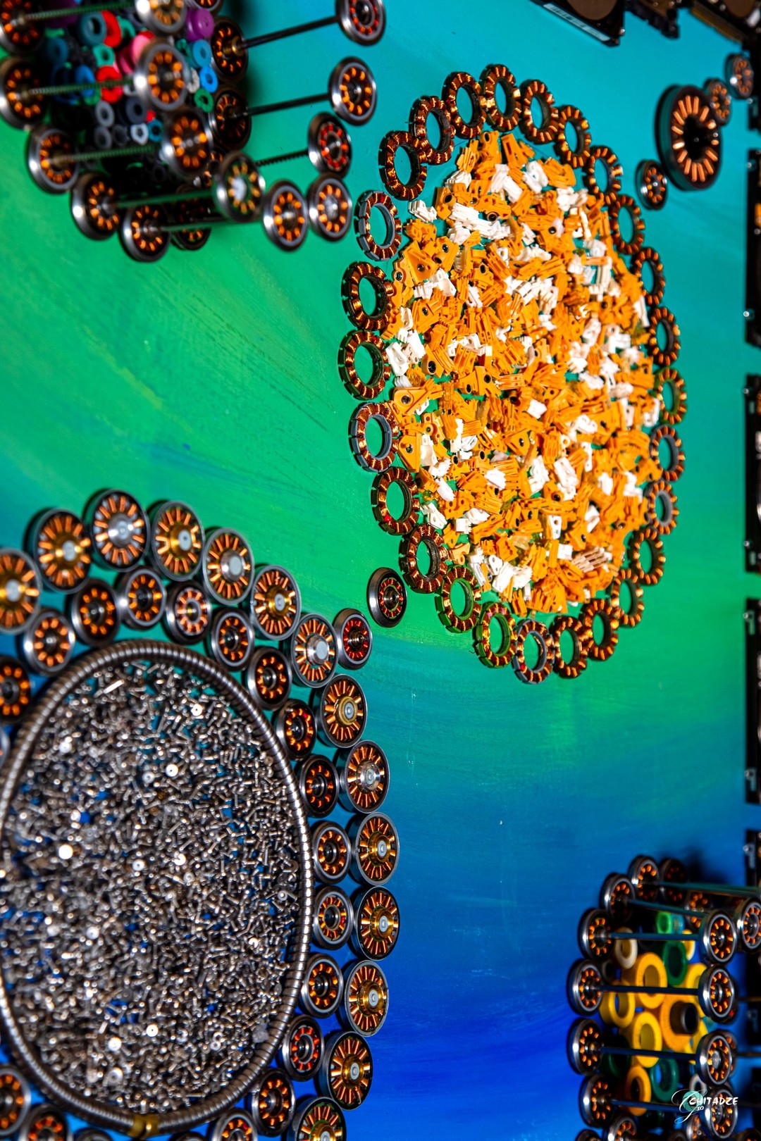 A circular arrangement of metallic discs surrounding a central dark cluster, set against a vibrant blue and green background.