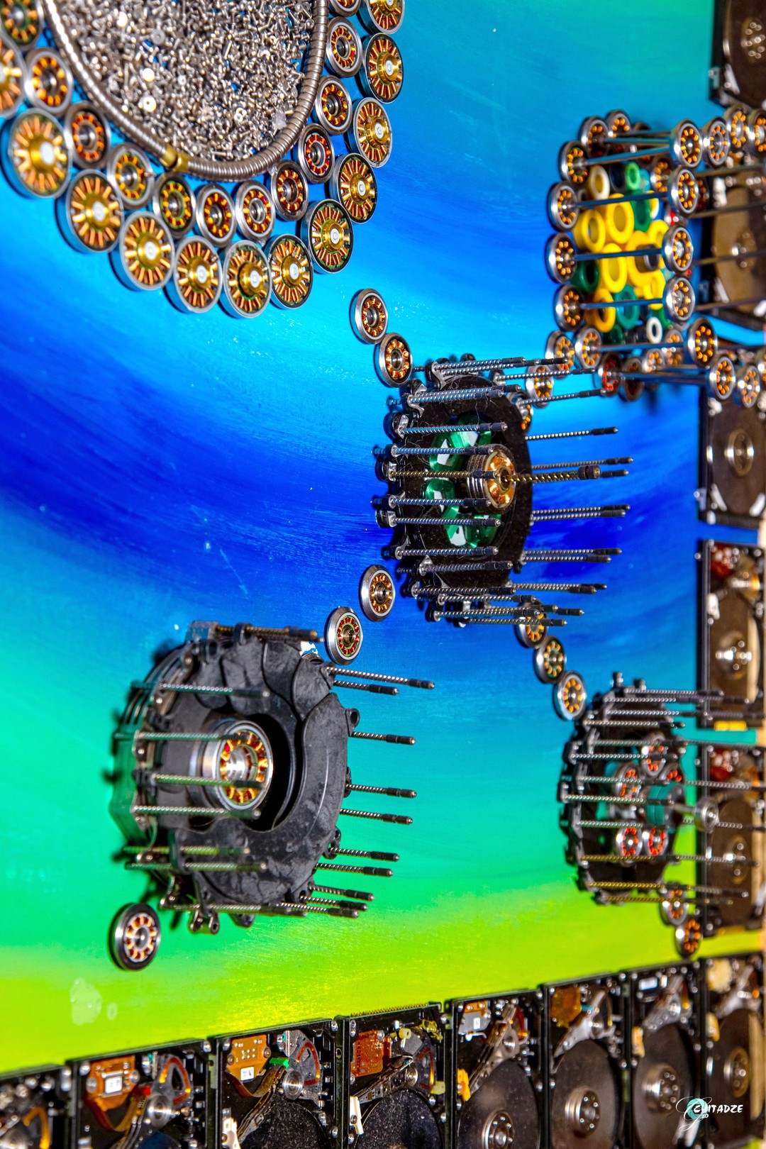 A circular arrangement of metallic discs surrounding a central dark cluster, set against a vibrant blue and green background.