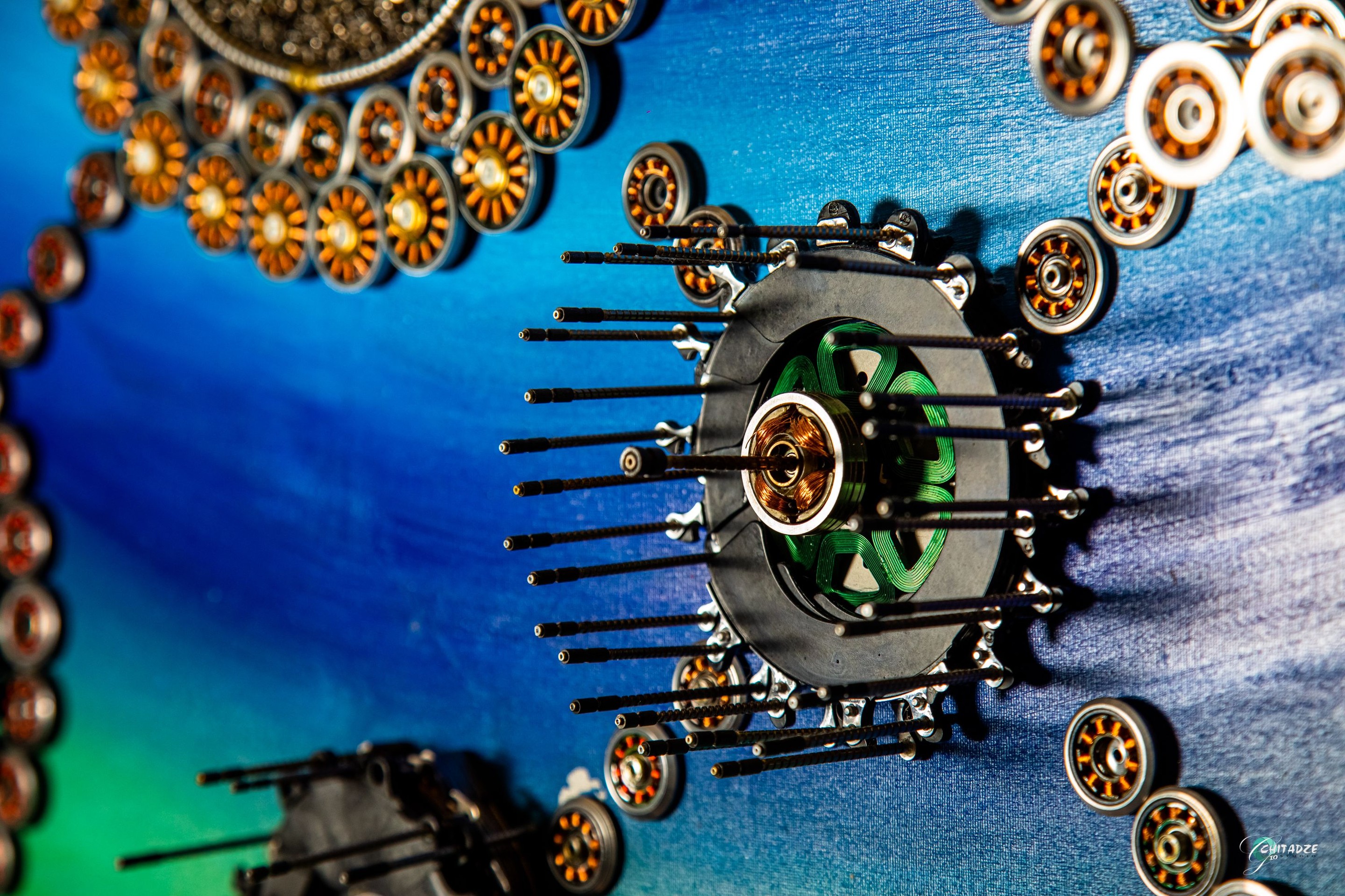 A circular arrangement of metallic discs surrounding a central dark cluster, set against a vibrant blue and green background.