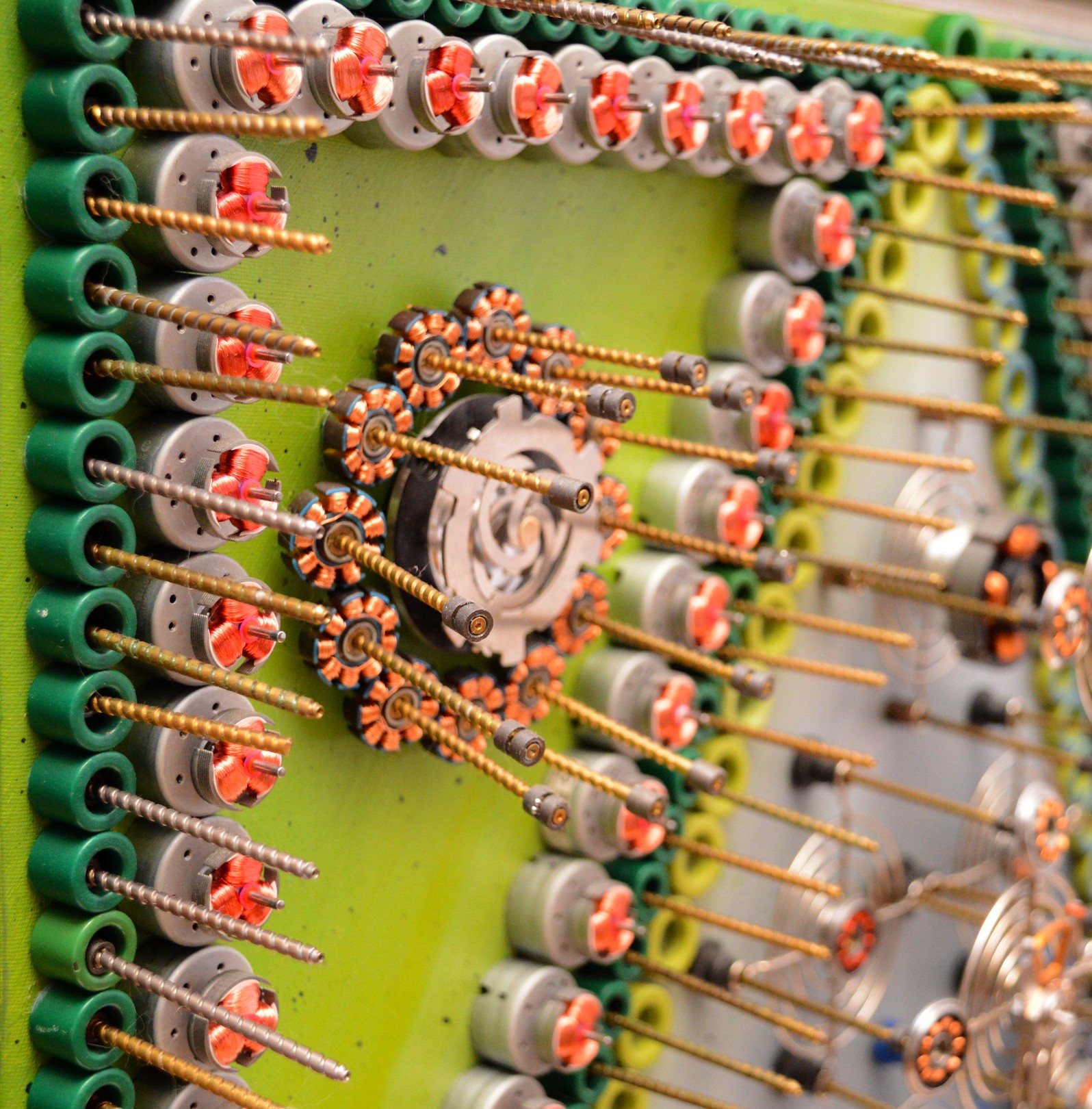 A mechanical collage featuring a grid of metallic figures surrounded by coiled springs and small gears.