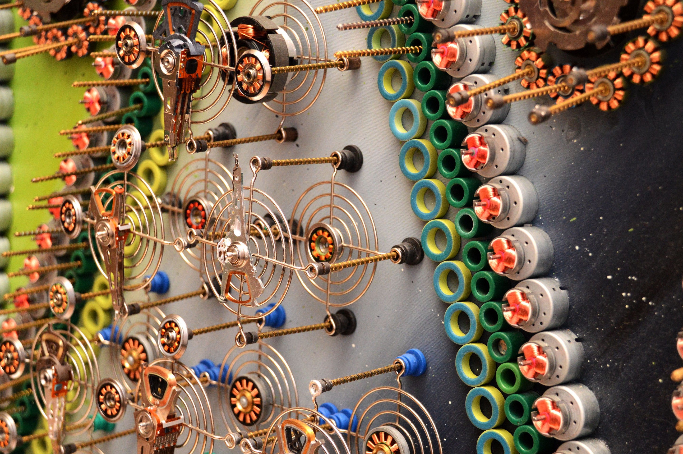 A mechanical collage featuring a grid of metallic figures surrounded by coiled springs and small gears.