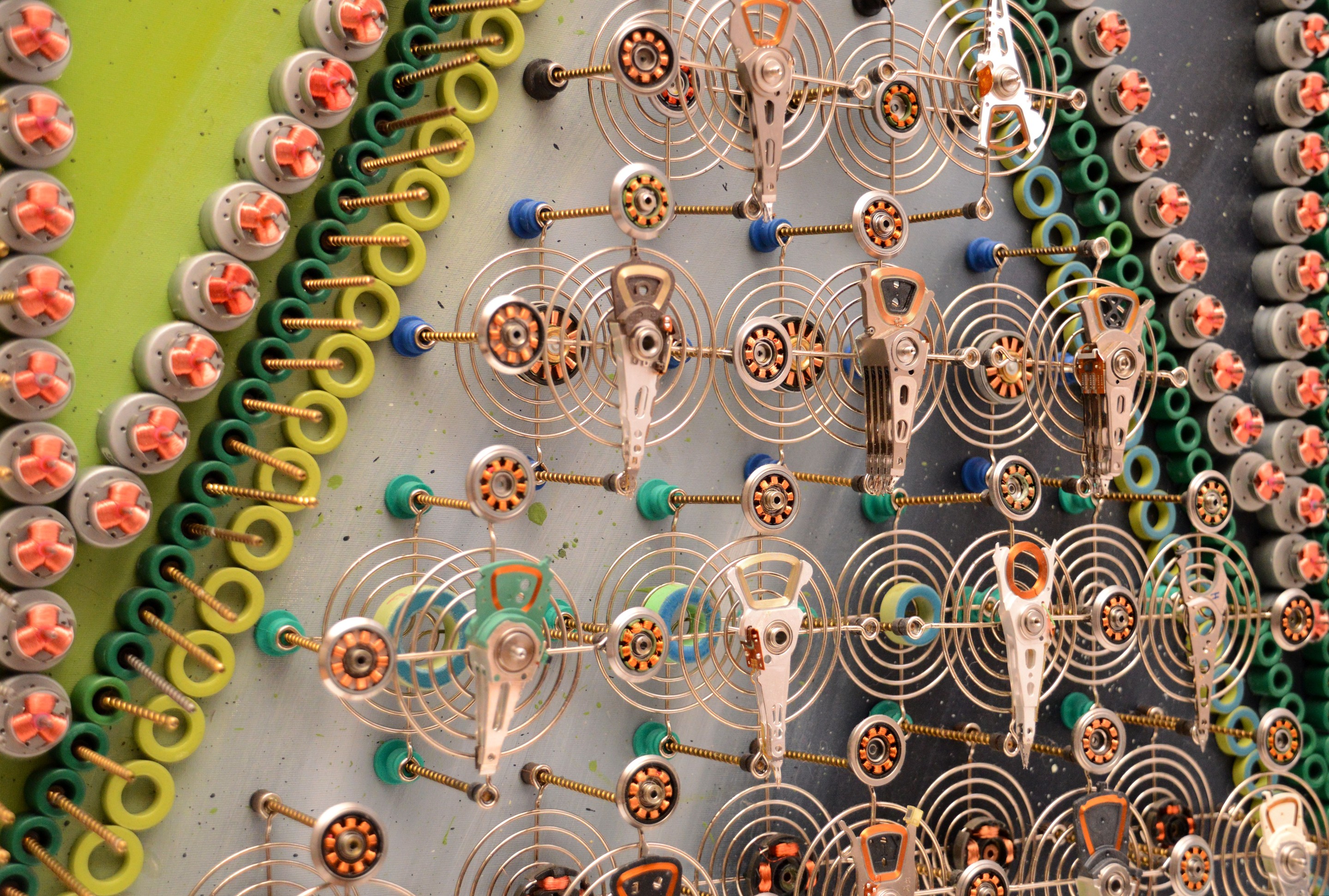 A mechanical collage featuring a grid of metallic figures surrounded by coiled springs and small gears.