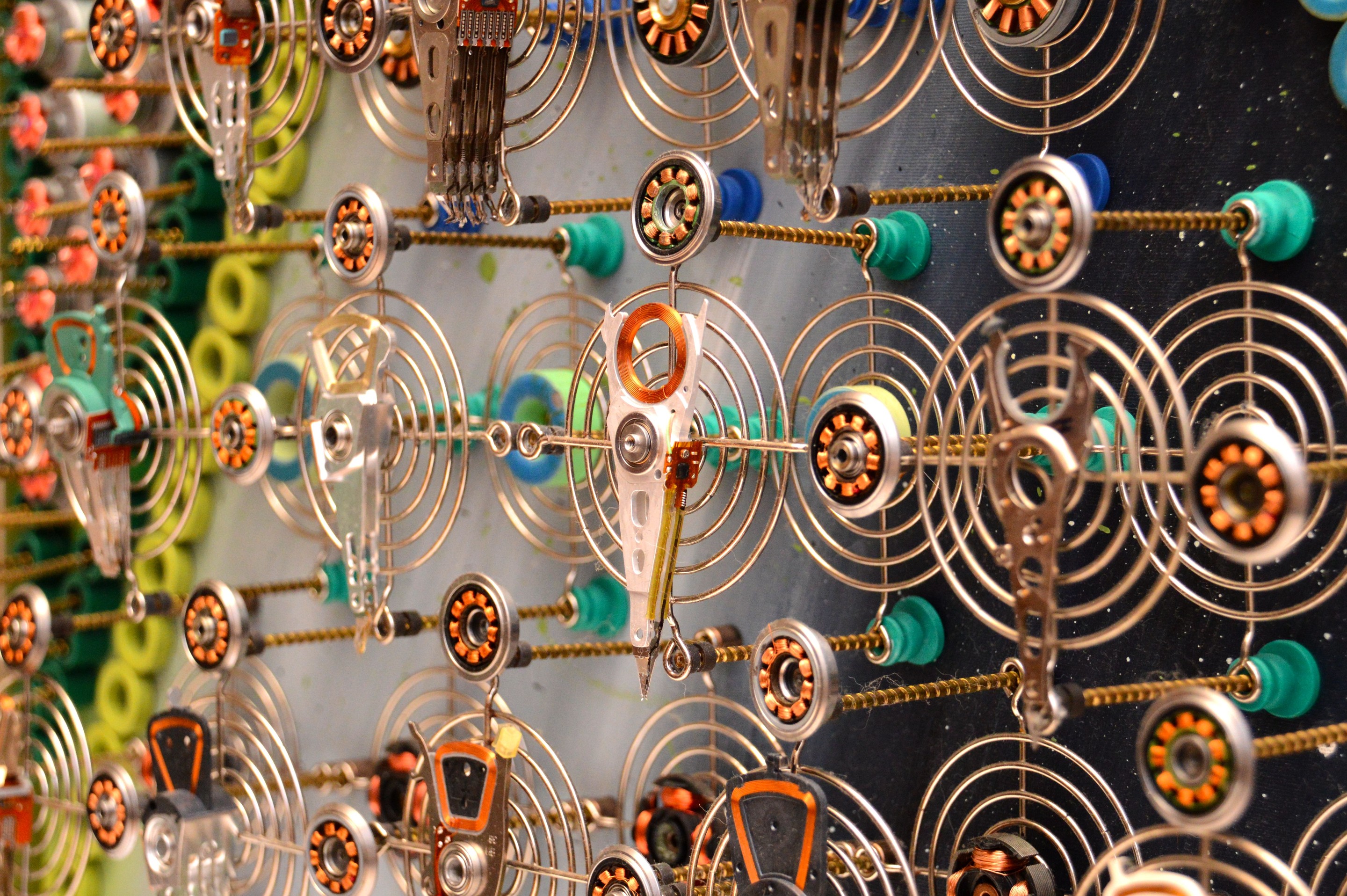 A mechanical collage featuring a grid of metallic figures surrounded by coiled springs and small gears.