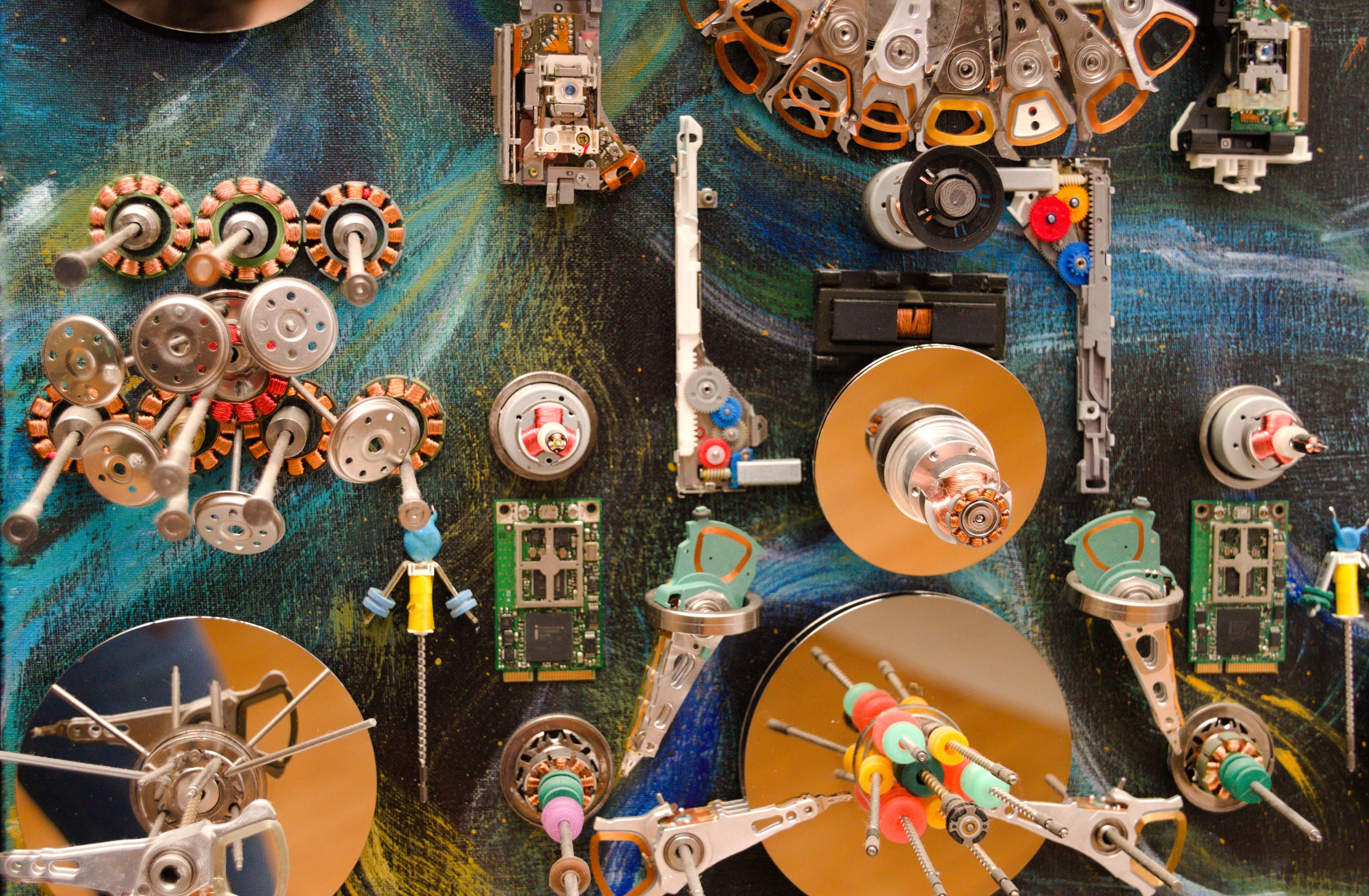 A chaotic collage of metallic mechanical parts and circuit boards scattered across a swirling blue background.