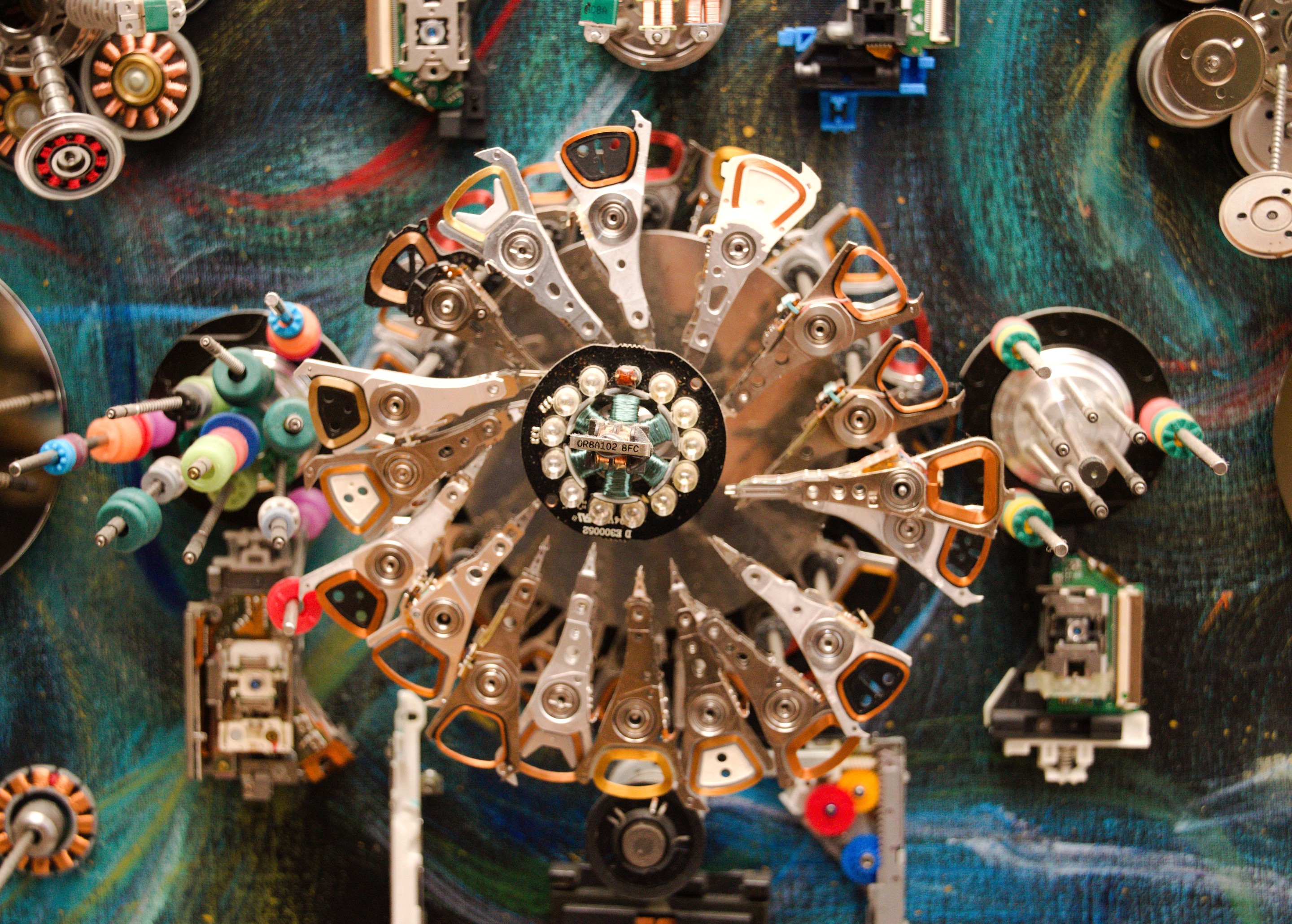 A chaotic collage of metallic mechanical parts and circuit boards scattered across a swirling blue background.