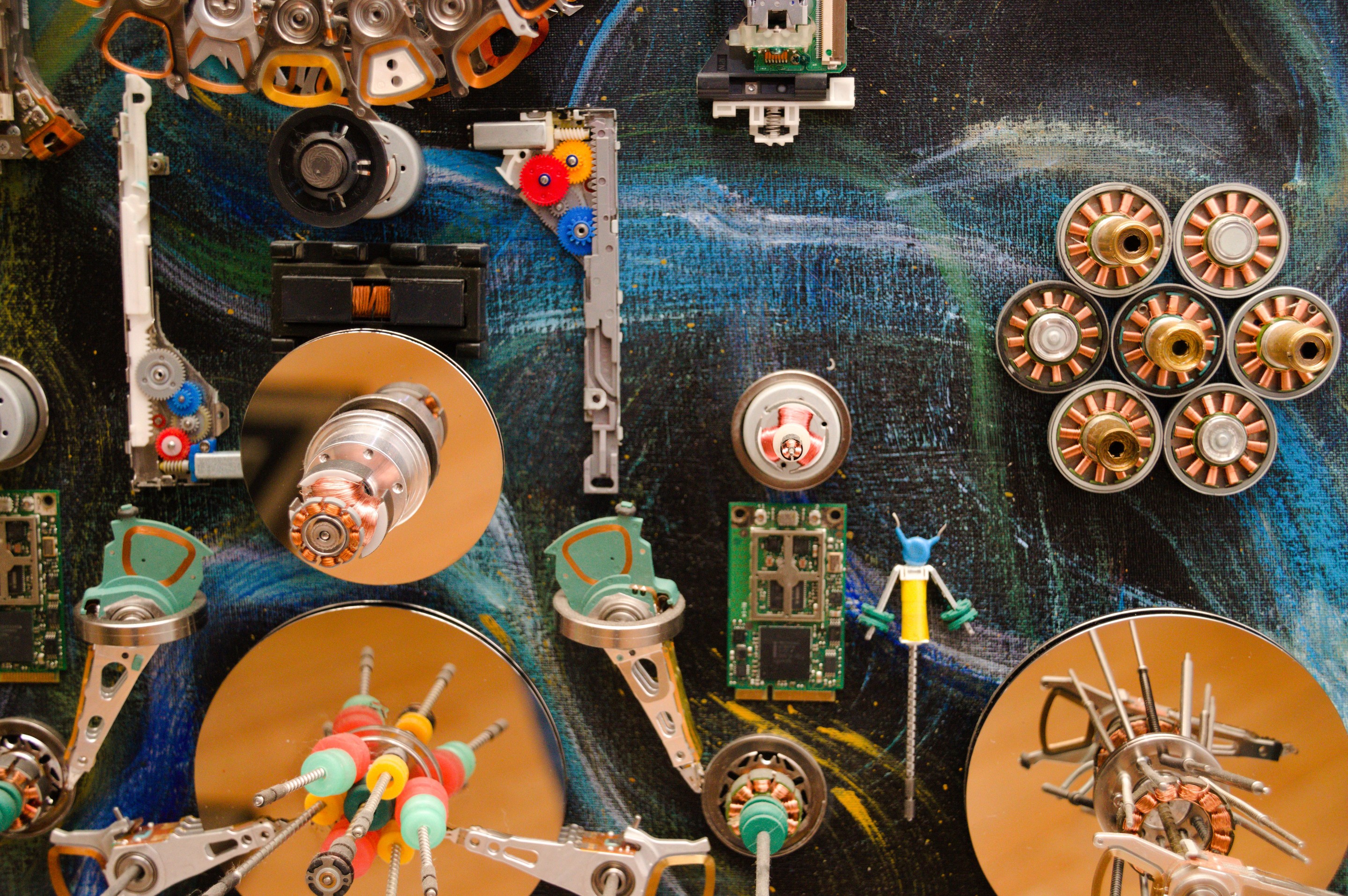 A chaotic collage of metallic mechanical parts and circuit boards scattered across a swirling blue background.