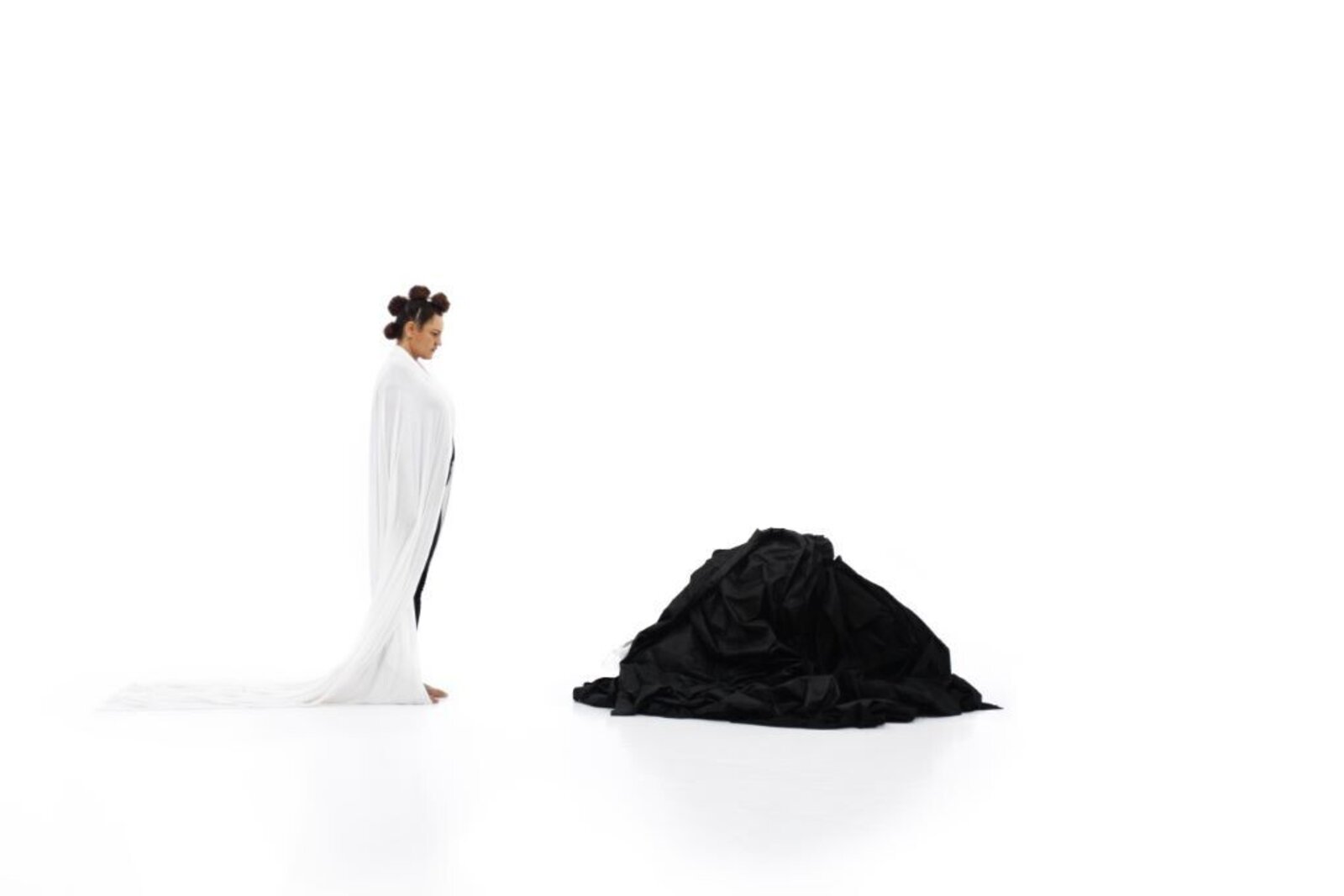 A minimalist composition contrasting a standing figure in white with a pile of black fabric.