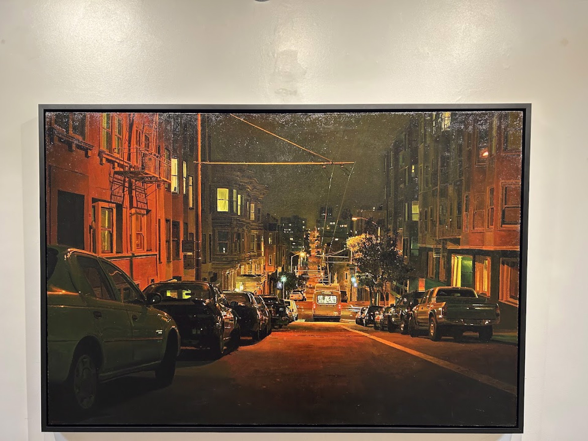 A painting of a city street at night with cars parked on the side of the road.