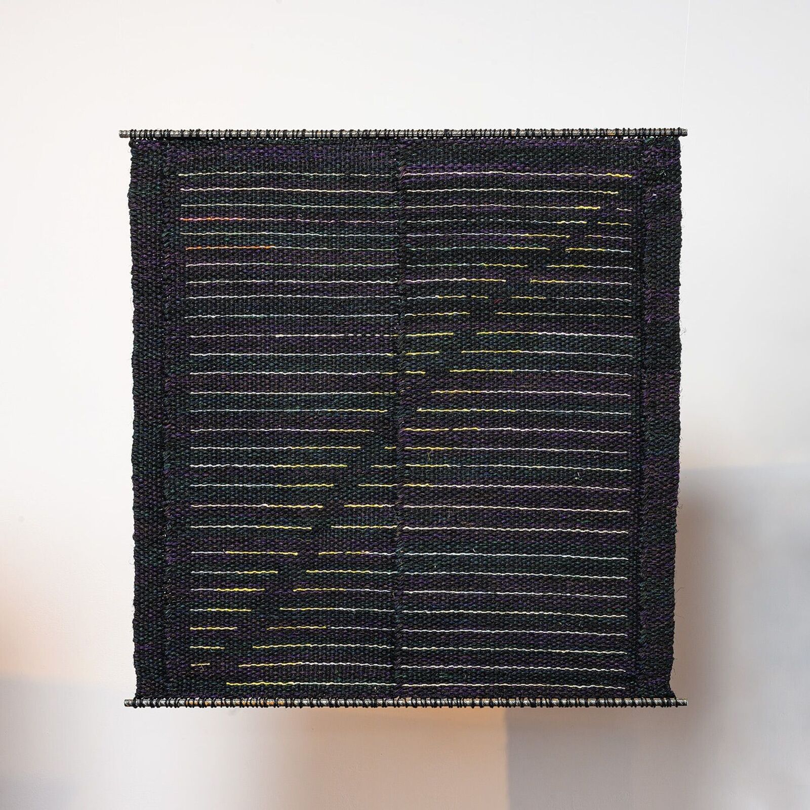 A woven textile artwork featuring a dark background with horizontal lines of white and yellow threads.