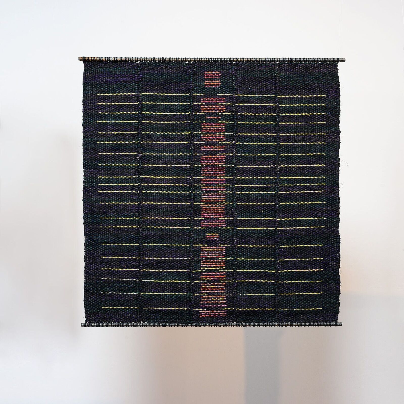 A woven textile featuring a central vertical motif of pink and red blocks against a dark background with horizontal yellow lines.