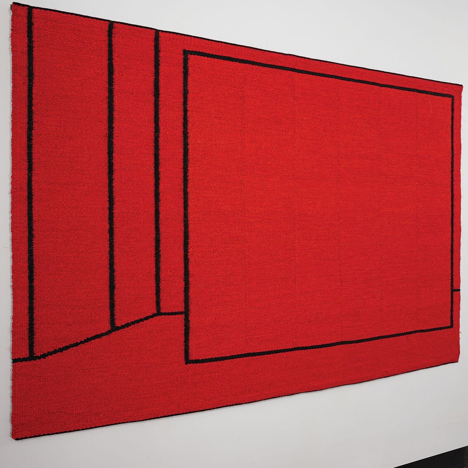 A bold red textile artwork featuring black geometric lines displayed in a gallery space.