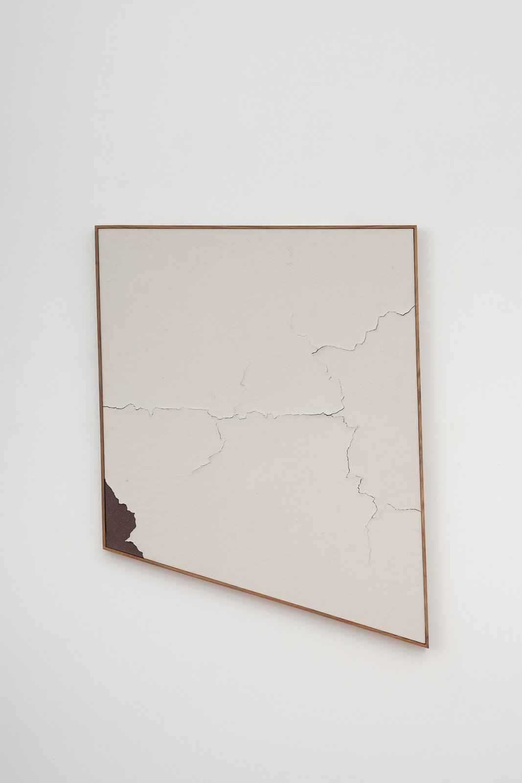 A minimalist artwork featuring a cracked, off-white surface within a wooden frame.