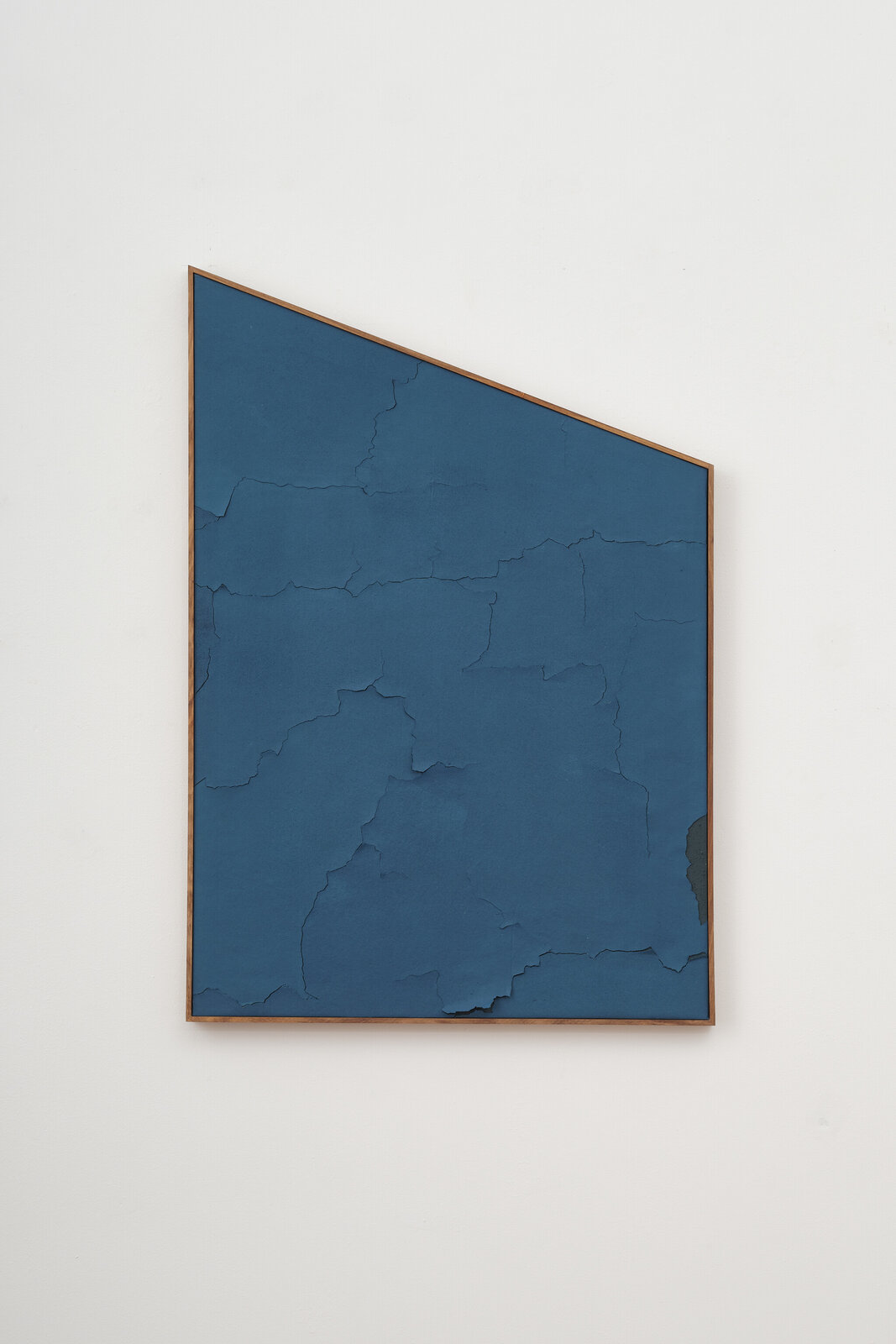 A framed abstract artwork featuring a textured blue surface with visible cracks and peeling layers.