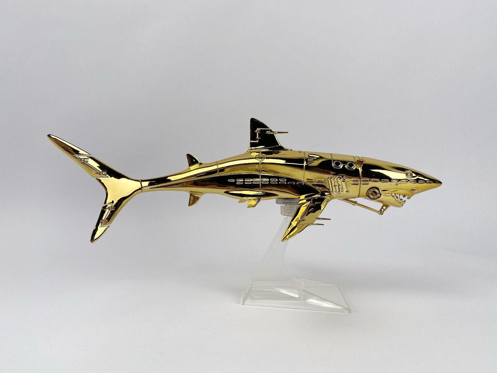 A gold model of a shark on a clear stand.