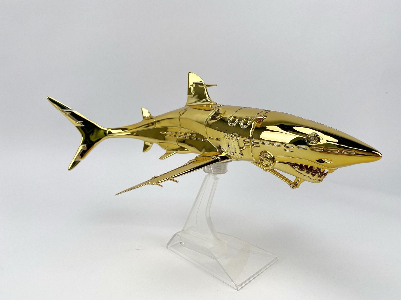 A gold model of a shark on a clear stand.
