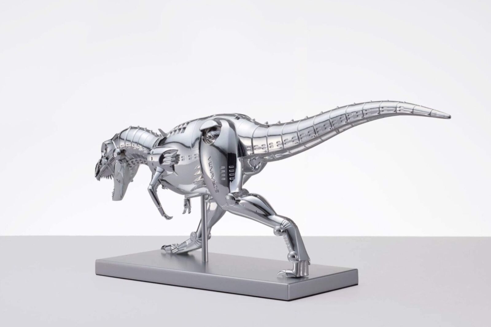 A metal model of a t-rex on a white surface.